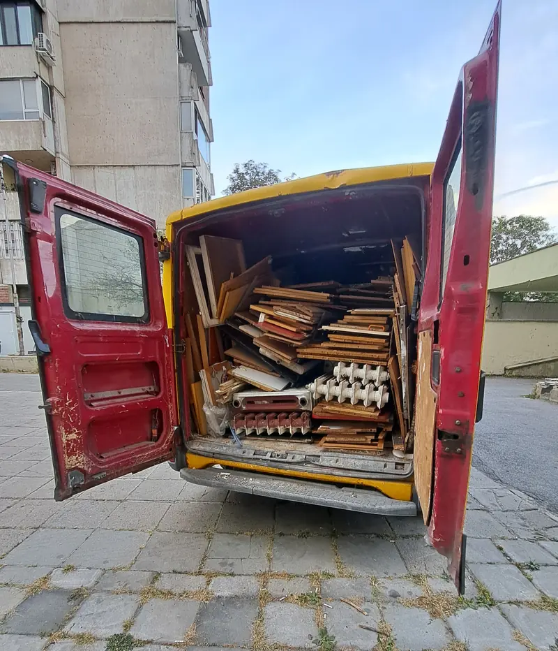 Жълтият бус на Хамалски услуги Мустафа с отворени врати, натоварен с дървени отпадъци и стари радиатори